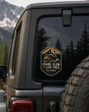Jeep with a 'Crawl Slow Live Free' sticker in a mountainous camping scene