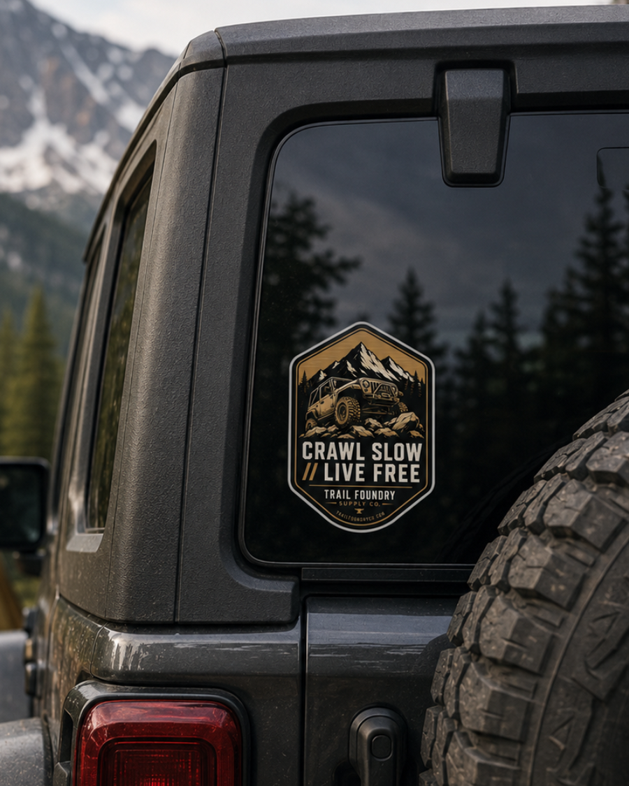 Jeep with a 'Crawl Slow Live Free' sticker in a mountainous camping scene